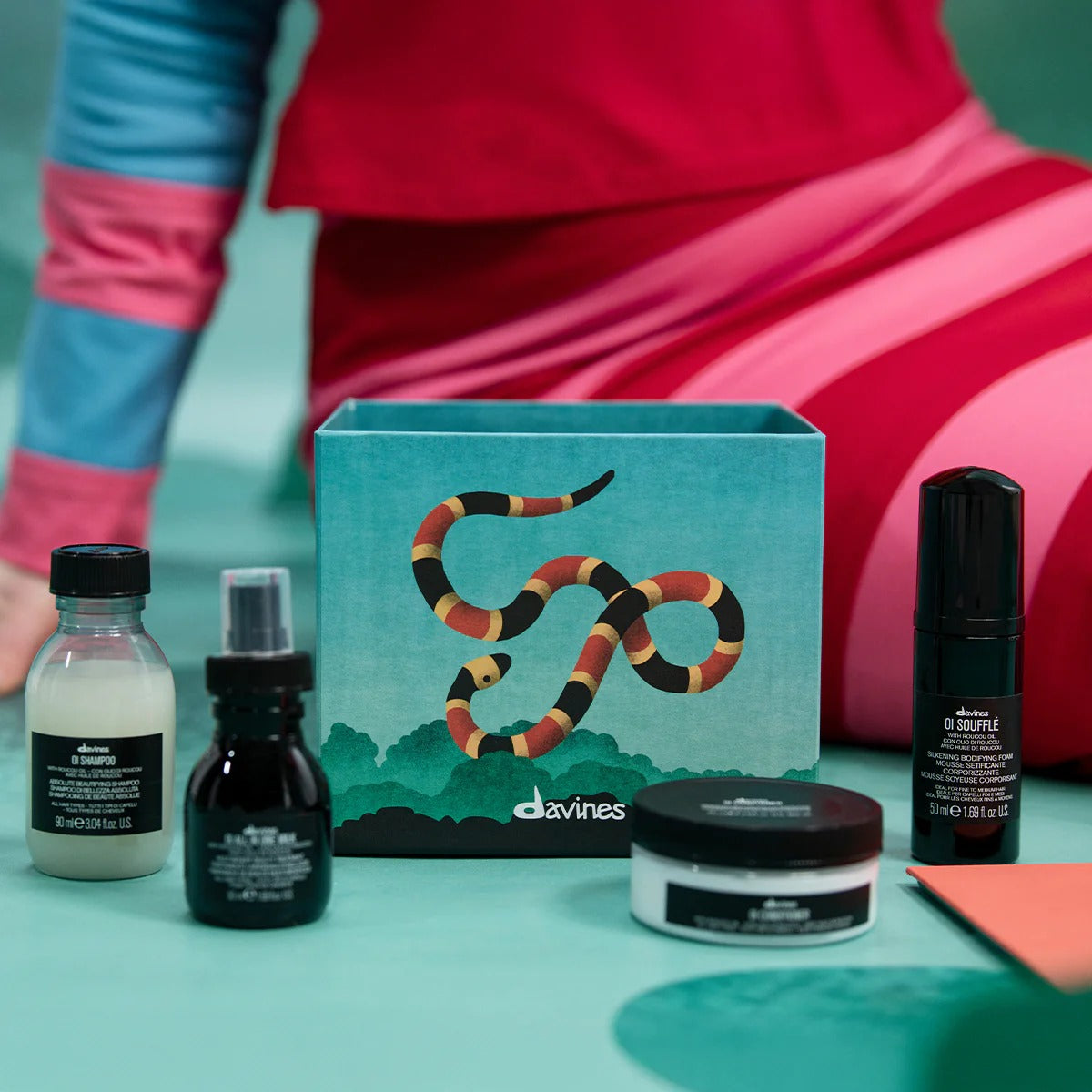 Produits du coffret Davines OI Discovery posés devant la boîte décorée d’un serpent coloré.