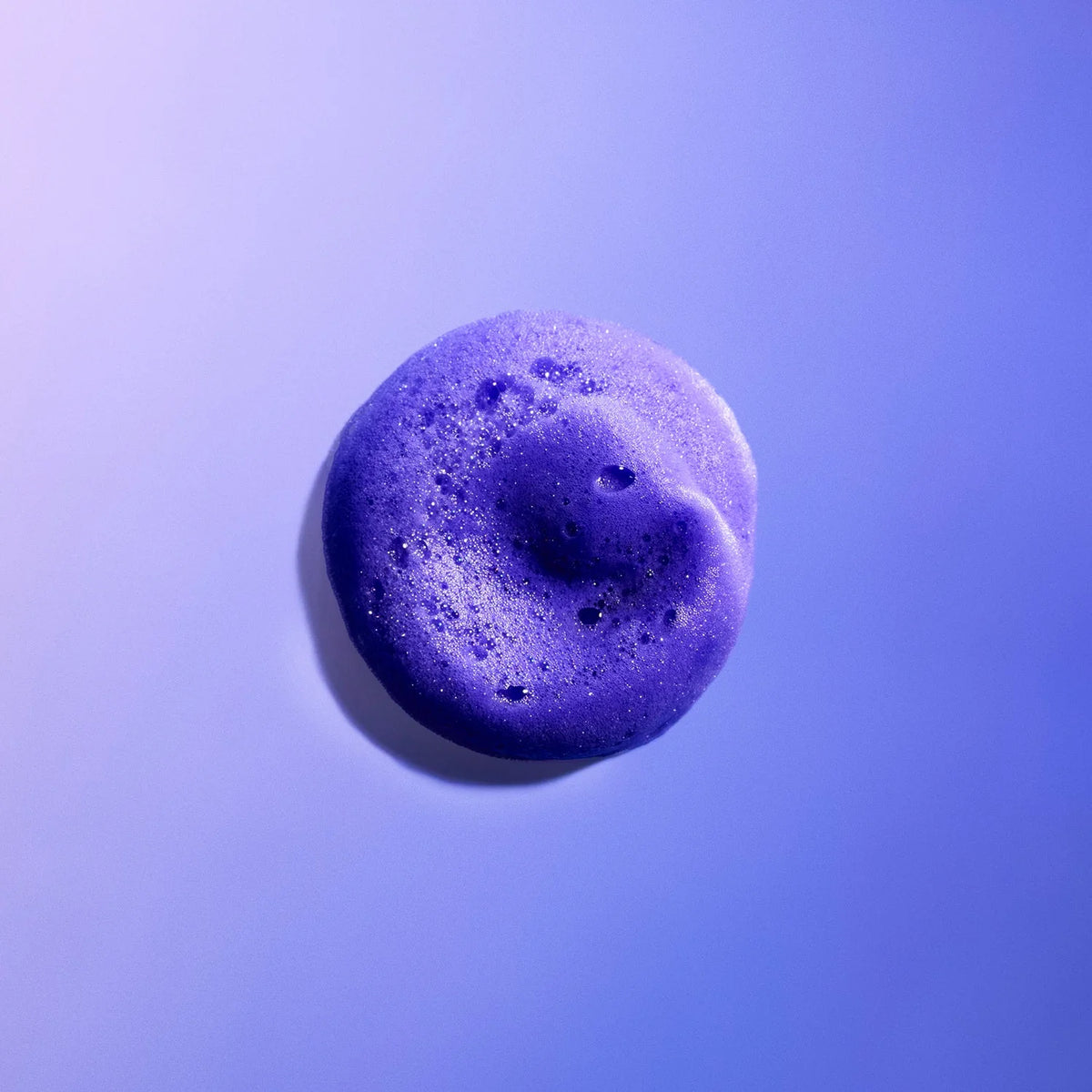 Gros plan sur une noisette de mousse violette K18 TripleBright, montrant sa texture aérée sur un fond mauve.