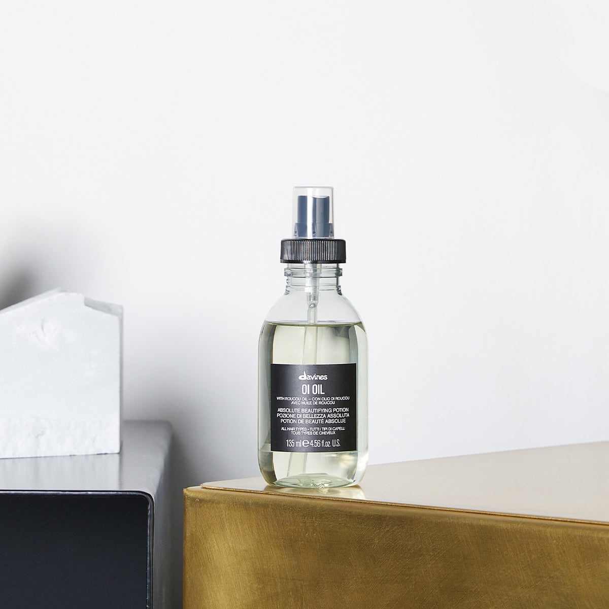 Bouteille de Davines OI Oil posée sur une surface dorée, montrant le produit dans un environnement moderne et élégant. Conçu pour tous les types de cheveux, cette huile beautifiante absolue apporte brillance et douceur instantanée.