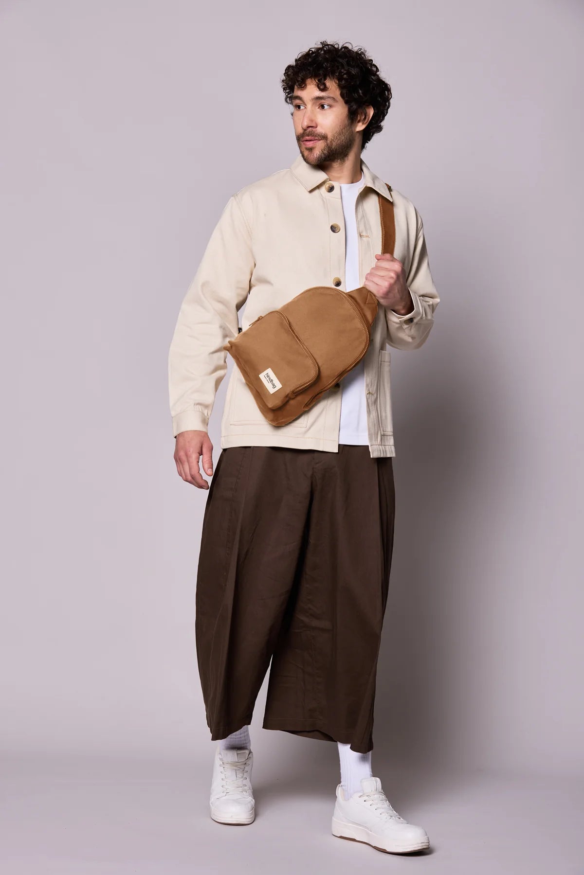 Hindbag Sling Bag Felix coloris Cannelle porté en bandoulière par un homme, sac compact unisexe pensé pour un usage urbain et quotidien