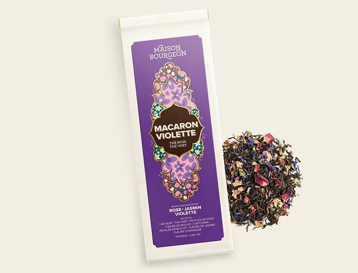 Image du produit "MACARON VIOLETTE" de la marque Maison Bourgeon, montrant un paquet de thé noir et vert aromatisé avec des saveurs de rose, de jasmin et de violette. Le paquet est à côté d'un mélange de thé en vrac, mettant en valeur les pétales de fleurs et les ingrédients naturels visibles dans le thé.