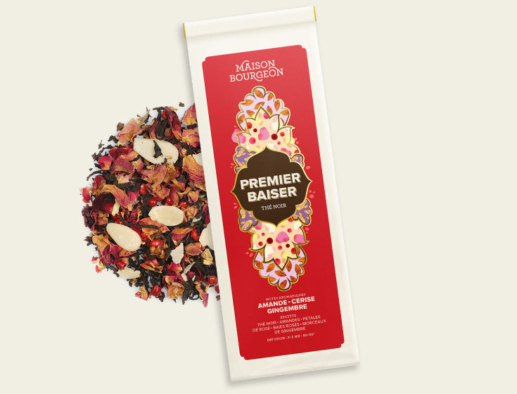 Paquet de thé noir Maison Bourgeon Premier Baiser avec des ingrédients visibles : amandes, pétales de rose, baies rouges et morceaux de gingembre.