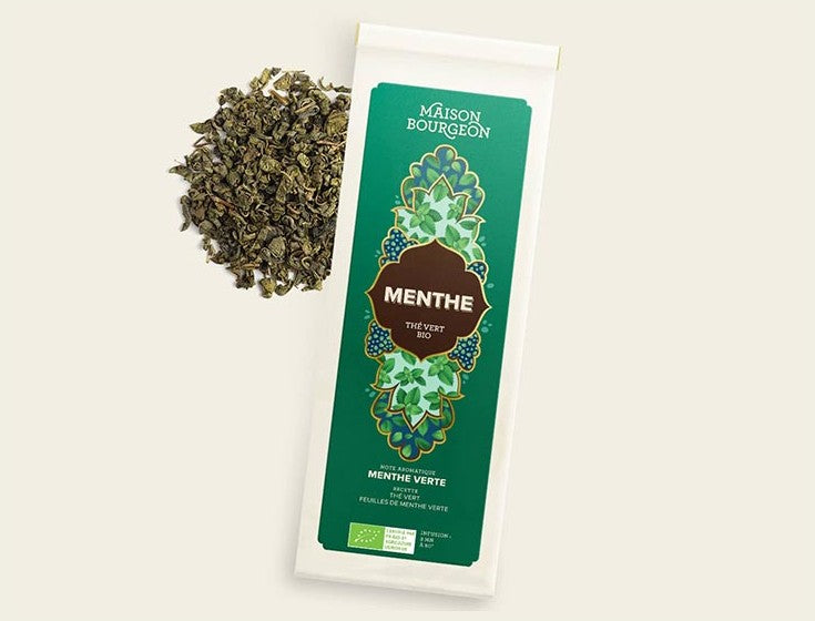 Image du produit "MENTHE" de la marque Maison Bourgeon, montrant un paquet de thé vert bio aromatisé avec de la menthe verte. Le paquet est à côté d'un mélange de thé en vrac, mettant en valeur les feuilles de menthe naturelles visibles dans le thé.