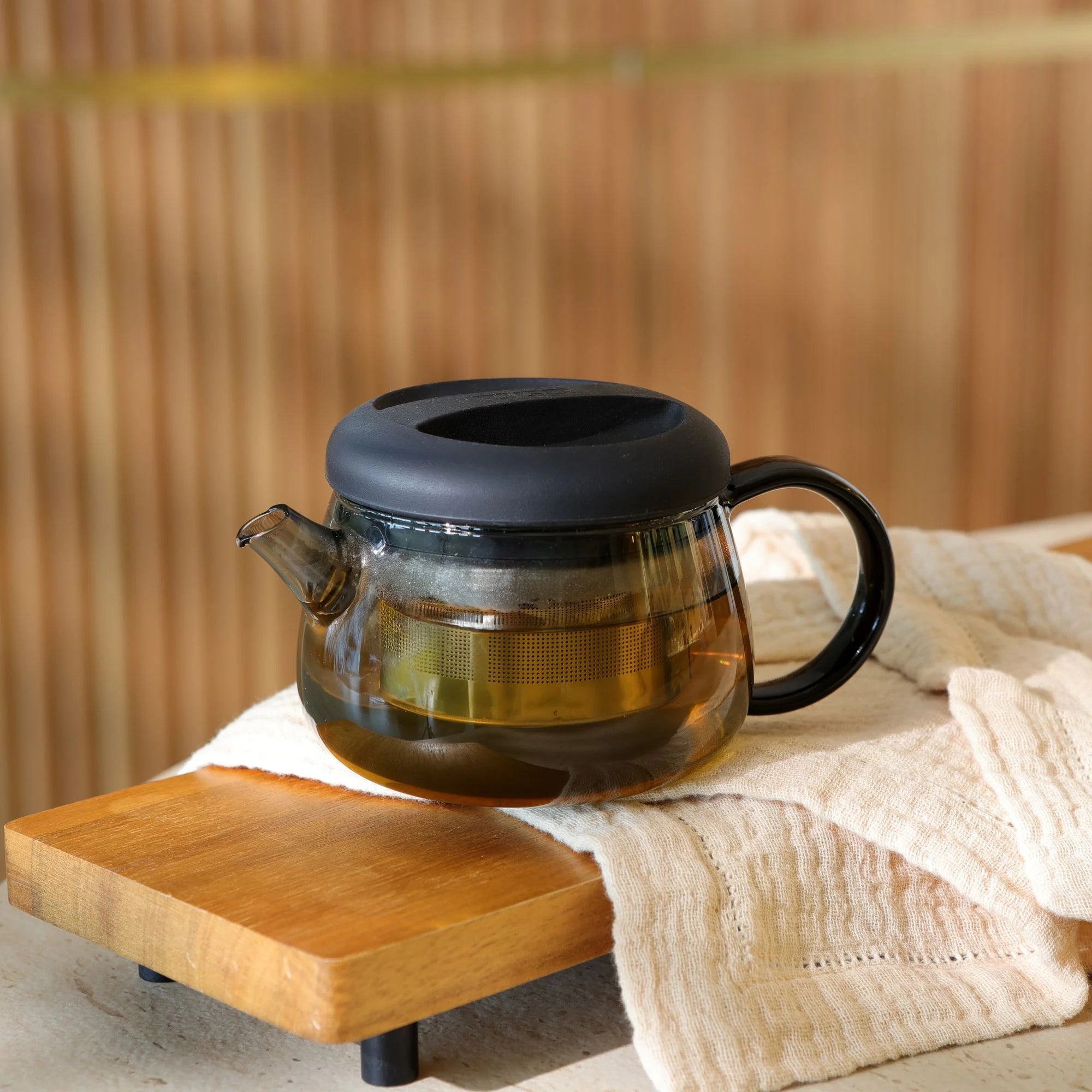 OGO Living Théière Fusion 300 ml en verre teinté avec filtre inox intégré, couvercle noir, anse et bec verseur, présentée avec du thé infusé