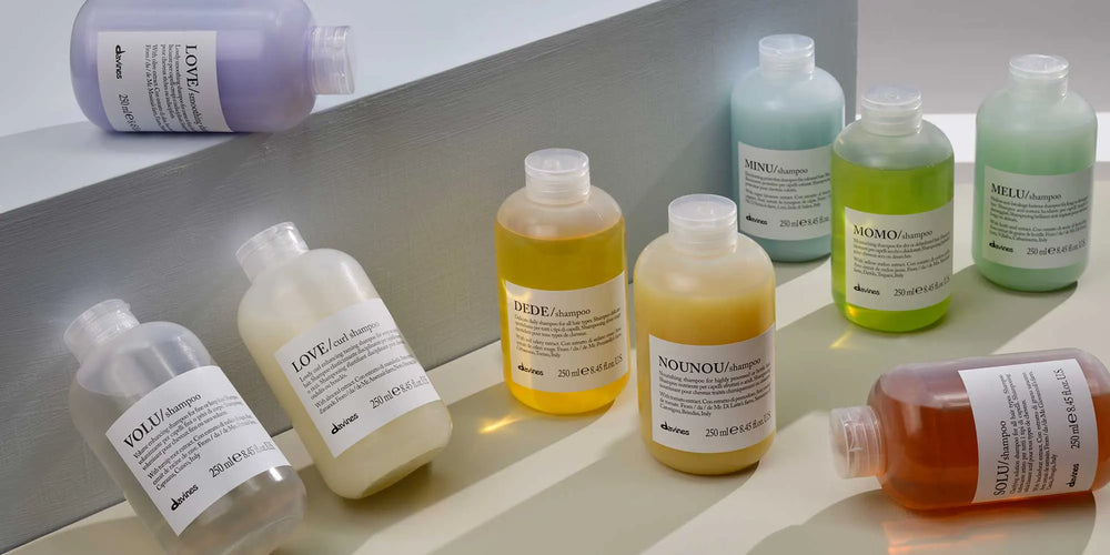 Flacons de shampooings Davines Essential Haircare aux couleurs des différentes familles, disposés sur un fond minéral clair.
