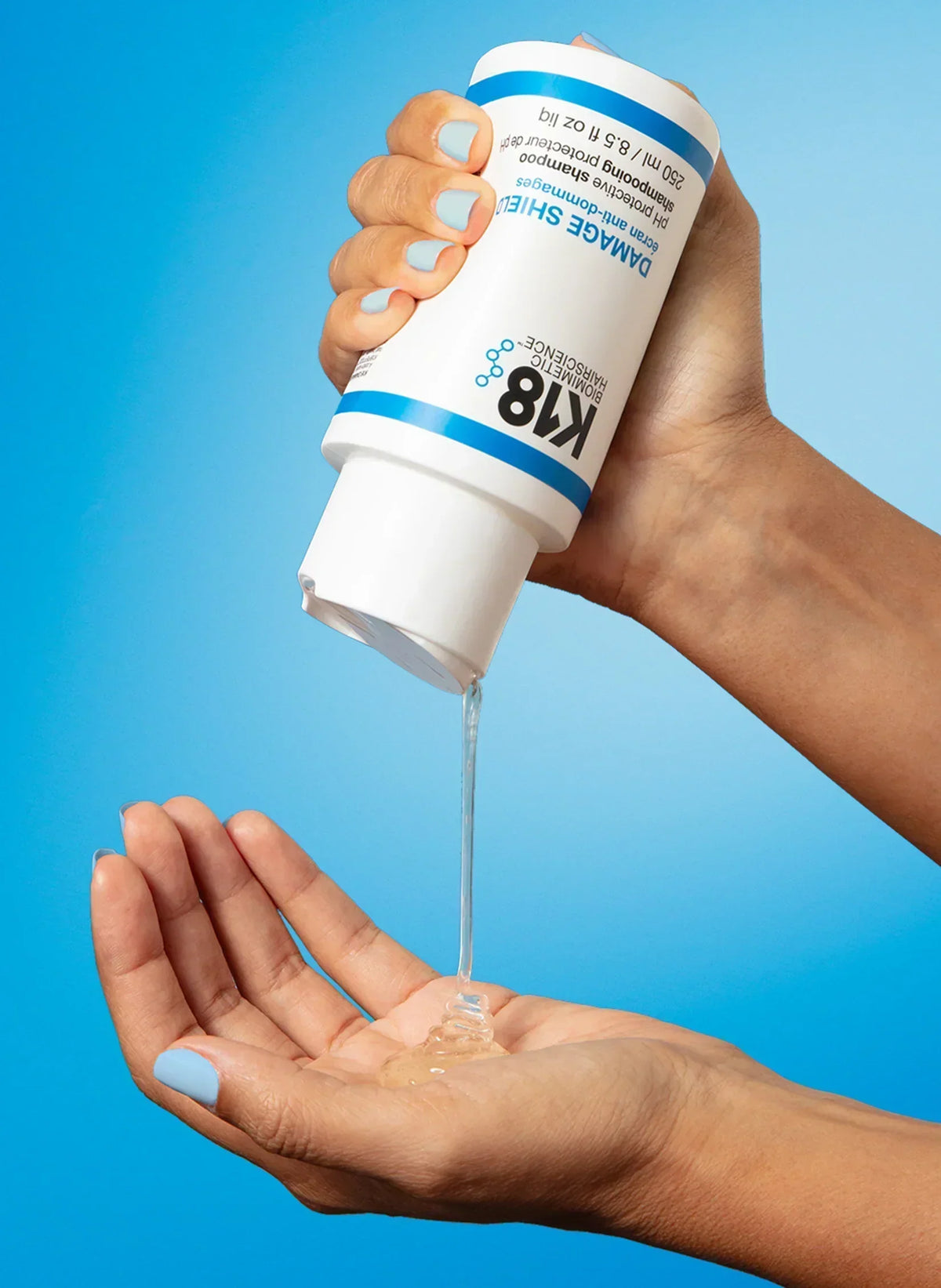 Shampooing K18 Damage Shield versé dans la paume de la main depuis un flacon de 250 ml sur fond bleu.