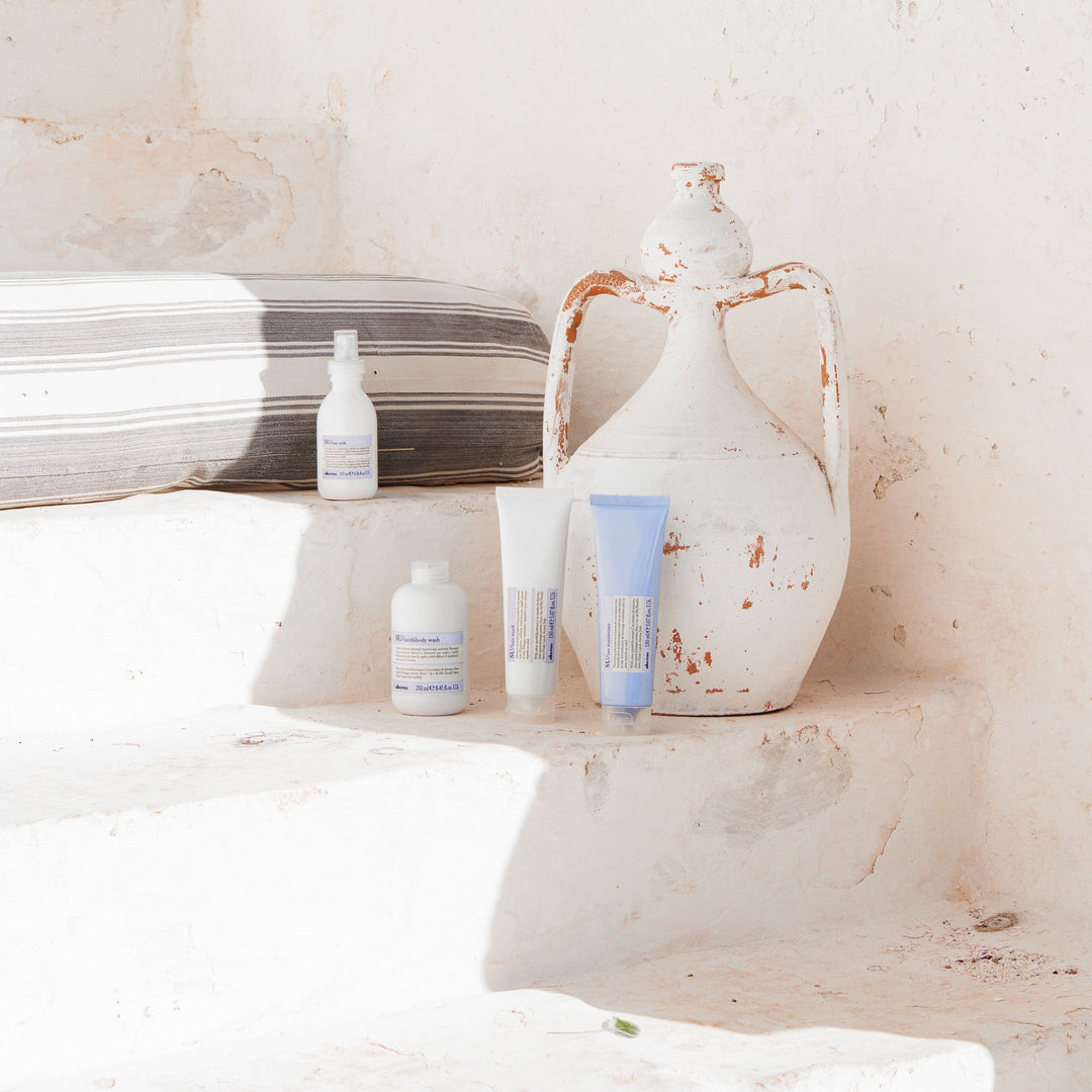 Trois produits capillaires SU de Davines disposés sur un rebord en pierre sous un soleil estival, avec le Hair & Body Wash, le Hair Mask et le Hair Milk