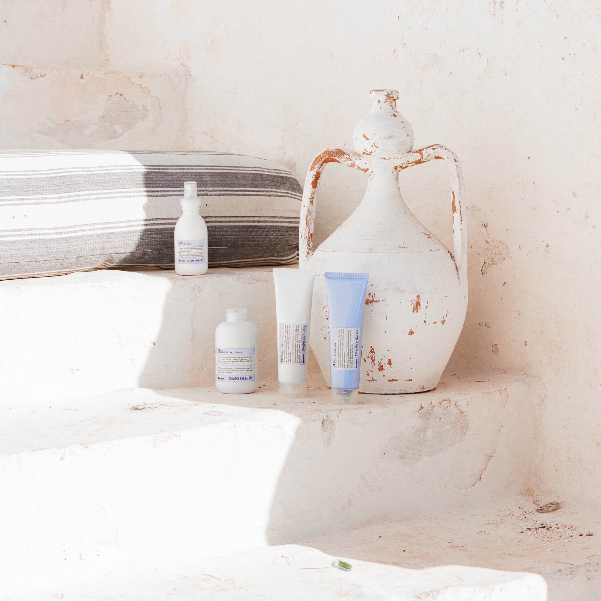 Trois produits capillaires SU de Davines disposés sur un rebord en pierre sous un soleil estival, avec le Hair & Body Wash, le Hair Mask et le Hair Milk