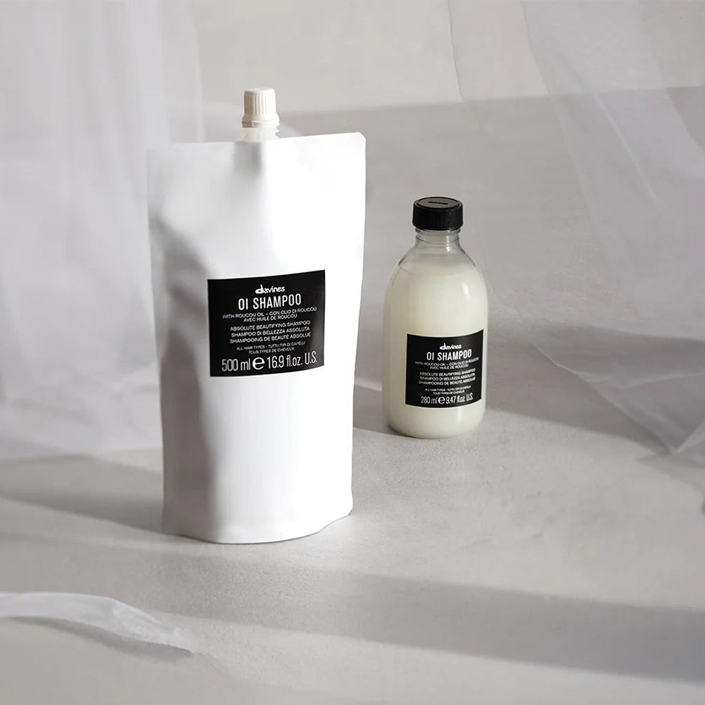 Éco-recharge Davines OI Shampoo 500 ml et flacon original 280 ml, vue rapprochée sur plan de travail minéral.