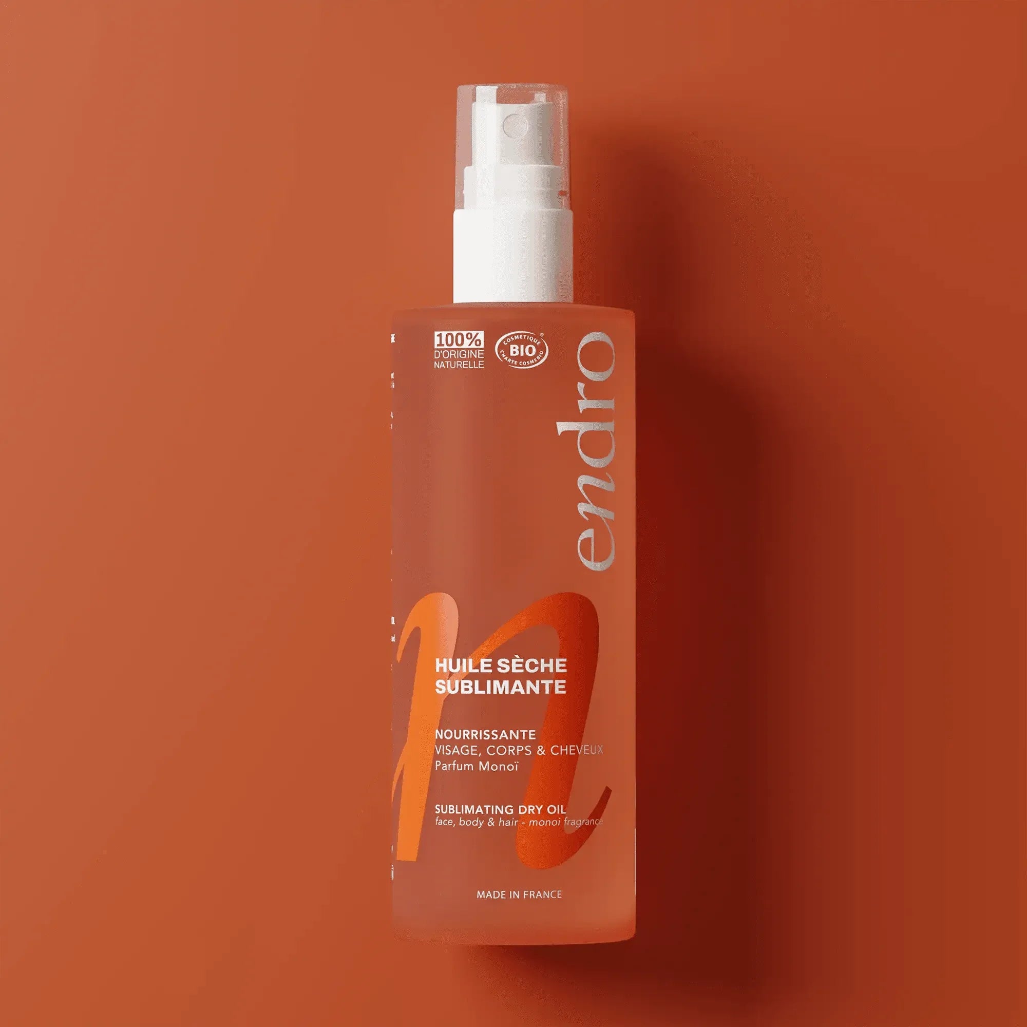 Flacon de l’huile sèche sublimante Endro Cosmétiques sur fond orange.