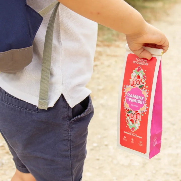 Enfant tenant un sachet d’infusion Ramène ta fraise Maison Bourgeon, boisson fruitée pratique et sans théine.