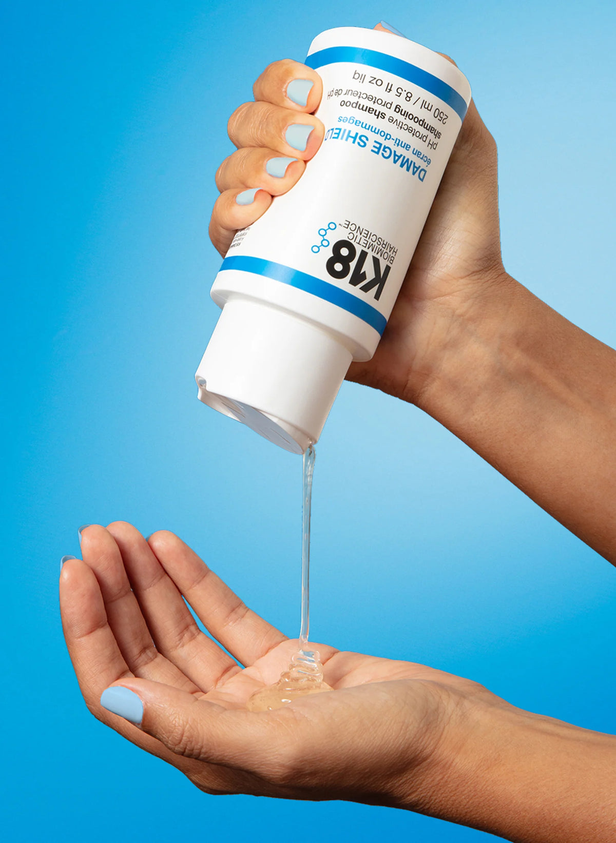 Texture du shampooing K18 Damage Shield versée dans la paume de la main depuis le flacon de 250 ml, sur fond bleu.