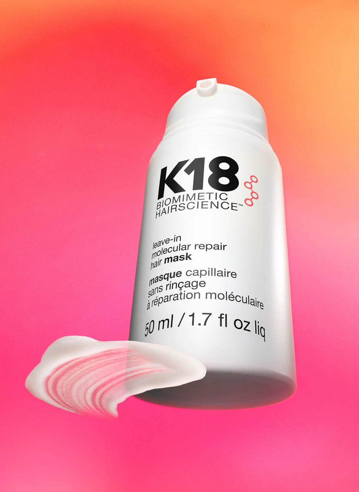 Flacon du masque K18 50 ml sans capuchon, accompagné d’une trace de crème blanche sur un fond dégradé rose et orange.
