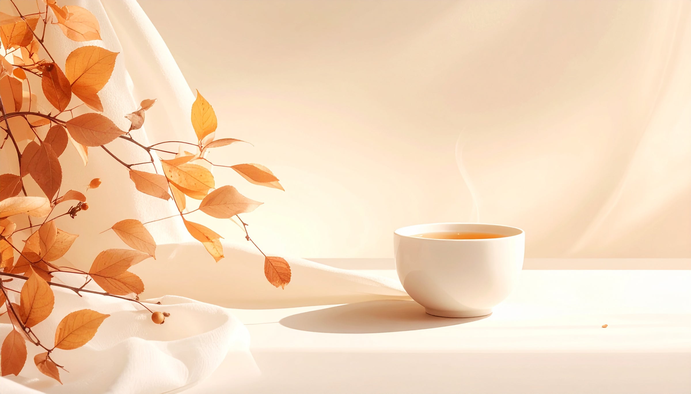 Tasse de the fumant posee sur une table ivoire, entouree de feuilles d automne dorees et d un tissu drape, creant une atmosphere douce et chaleureuse de rituel bien-etre.