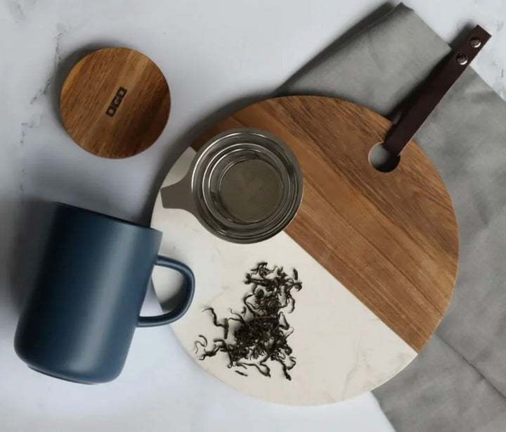 Tisaniere de 475 ml en gres bleu mat avec filtre inox et couvercle bois Ogo Living, vue du dessus avec feuille de the, sur planche en bois et marbre.