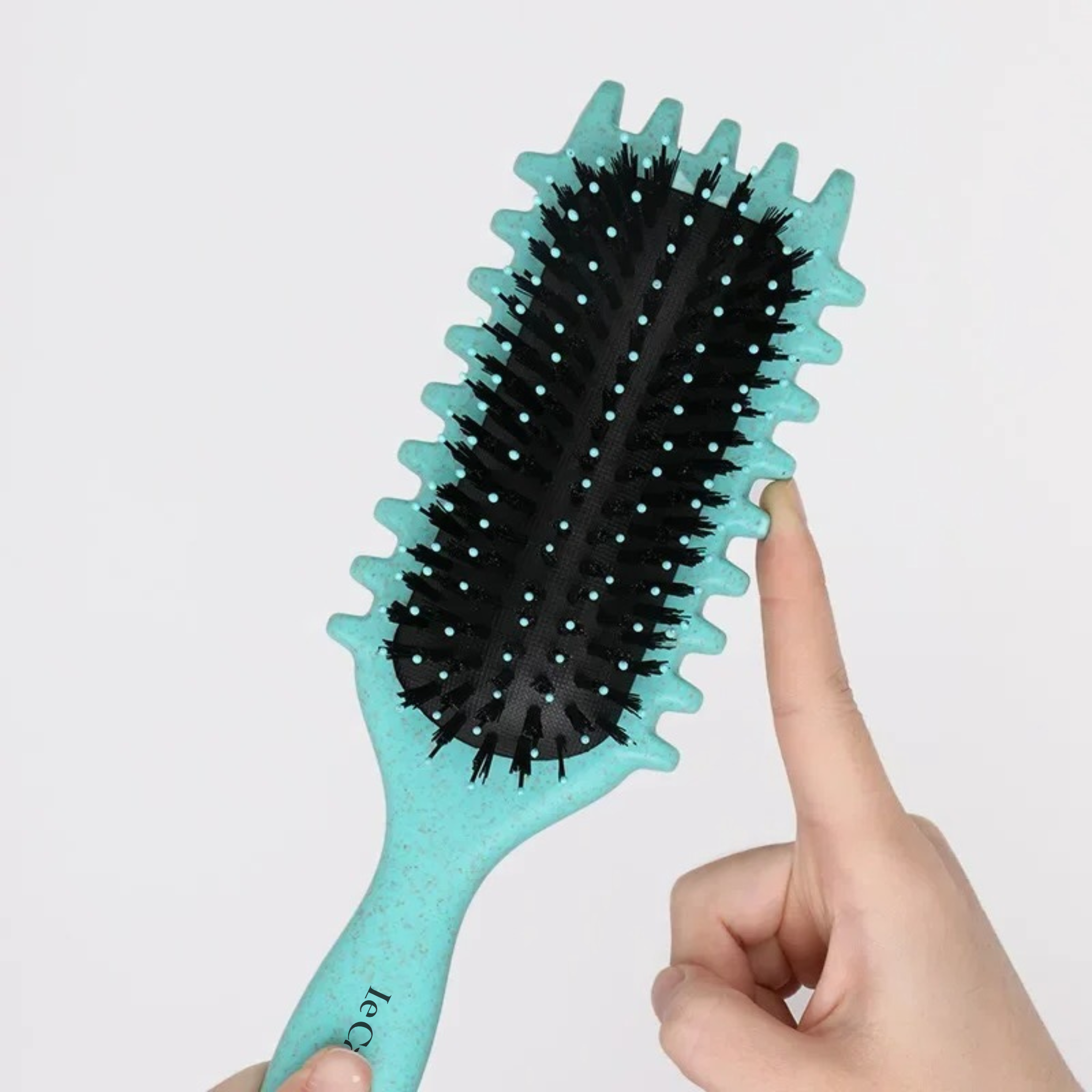 Gros plan sur la Brosse Définition Iconic Curl vert menthe : doigt démontrant la flexibilité des picots nylon et la douceur sur le cuir chevelu.