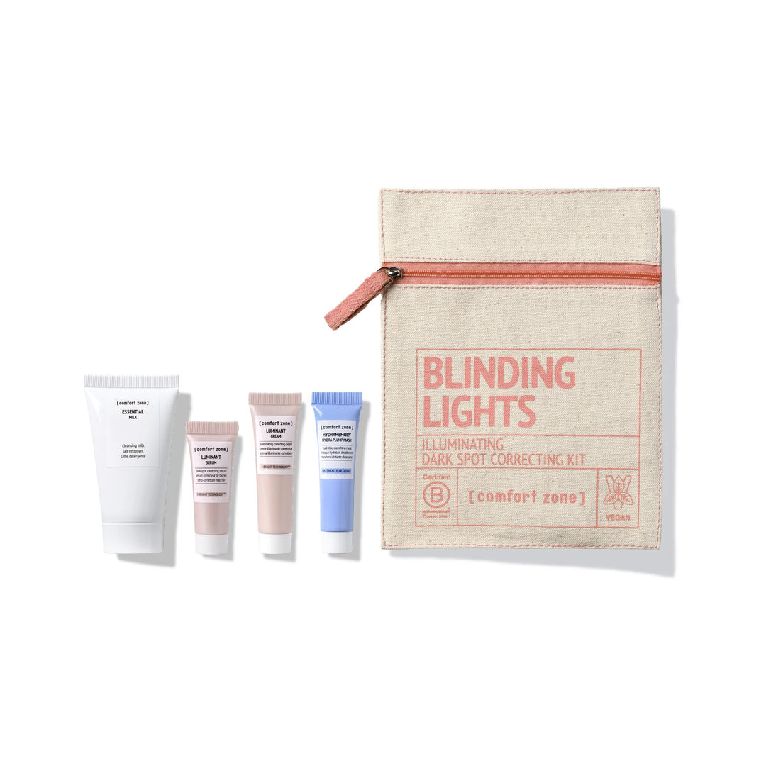 Coffret Blinding Lights Comfort Zone : trousse en coton beige zippée et quatre mini-soins visage (lait nettoyant Essential, sérum Luminant, crème Luminant, masque Hydramemory) alignés sur fond blanc, kit illuminateur correcteur de taches pigmentaires.
