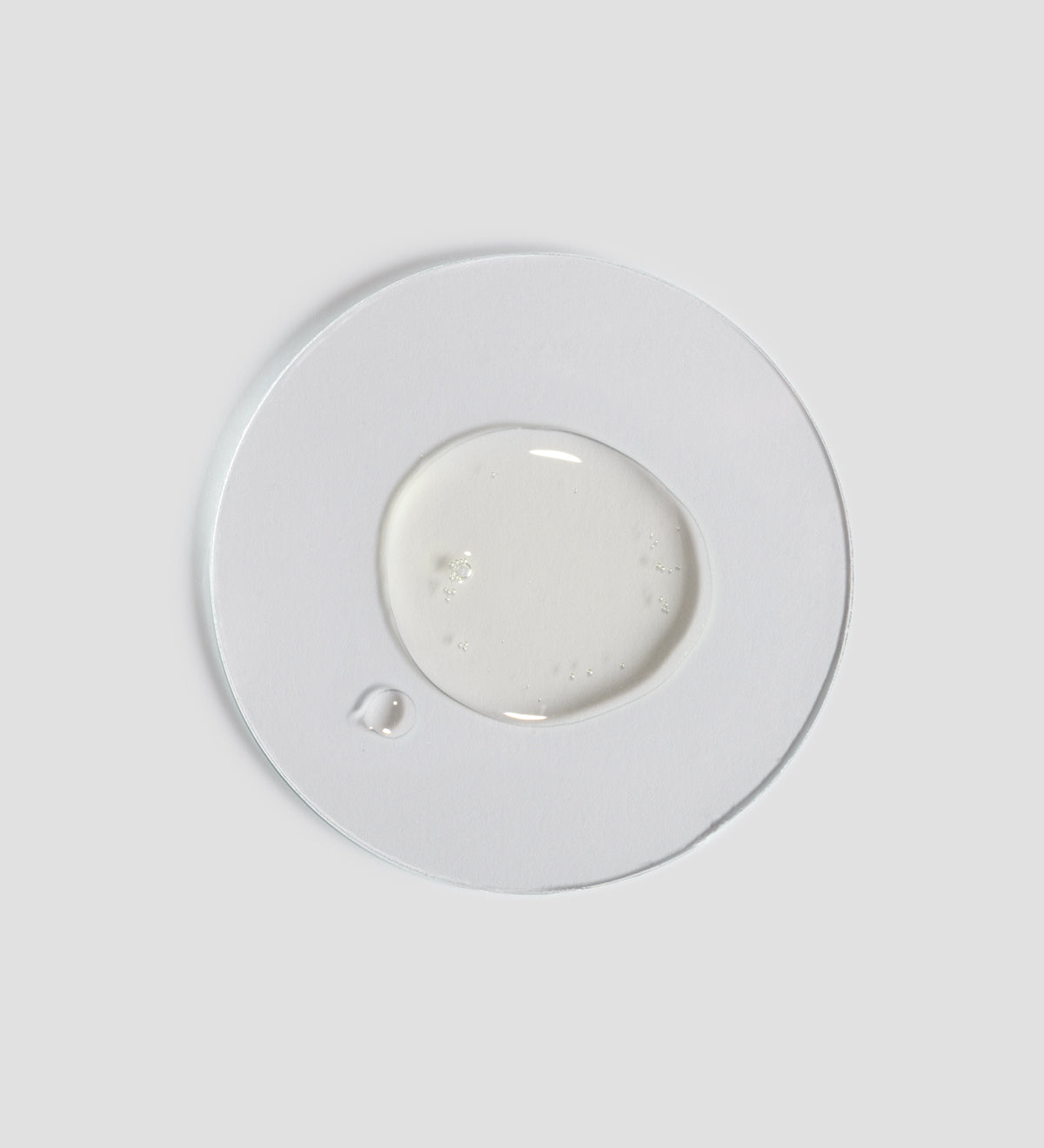Texture de l'huile pour le corps Comfort Zone Body Strategist. Une goutte d'huile claire sur une plaque circulaire transparente, montrant la consistance et l'apparence du produit.