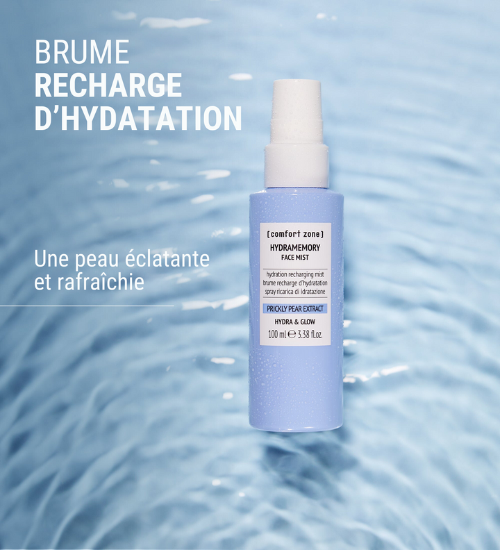 Image du Hydramemory Face Mist de [comfort zone] avec un fond d'eau ondulée bleu clair. Le produit est décrit comme une brume de recharge d'hydratation pour une peau éclatante et rafraîchie. Le texte sur l'image indique "Brume Recharge d'Hydratation" et "Une peau éclatante et rafraîchie".