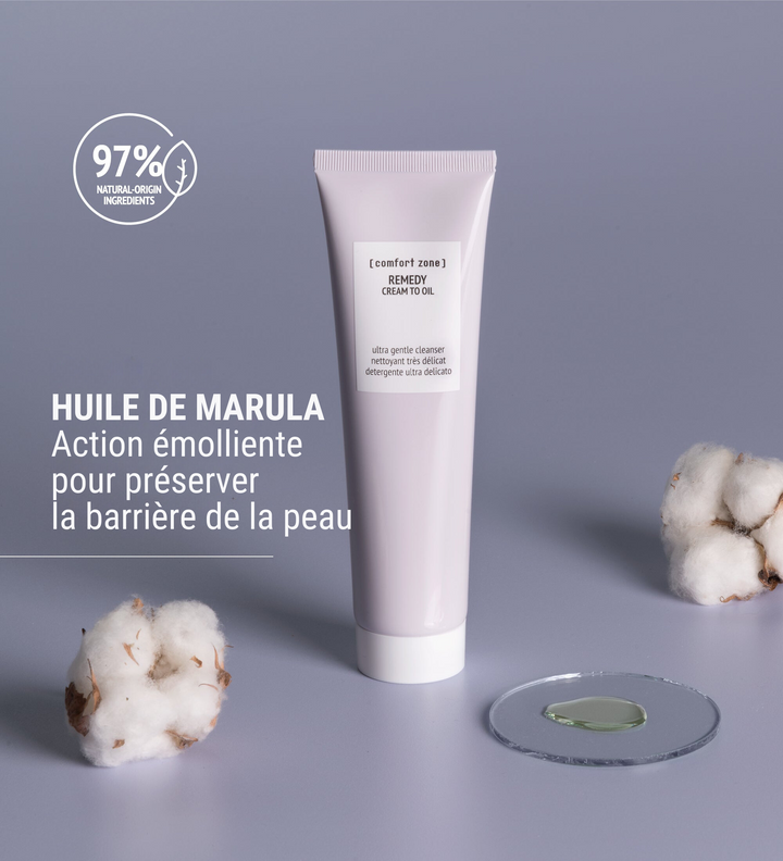 Affiche publicitaire du nettoyant ultra délicat [comfort zone] REMEDY Cream to Oil avec huile de Marula. Texte "Huile de Marula, action émolliente pour préserver la barrière de la peau" et un logo indiquant "97% d'ingrédients d'origine naturelle". Présentation du produit en tube, posé sur une surface grise avec des éléments décoratifs de coton et une goutte de produit sur une plaque transparente.
