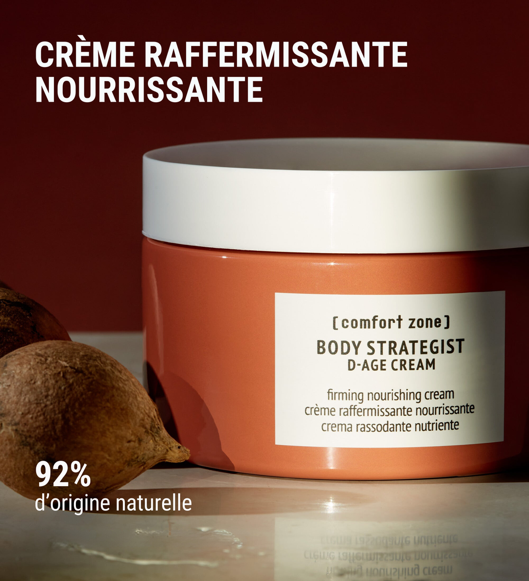 Pot de "Body Strategist D-Age Cream" de Comfort Zone avec des légumes à proximité, mettant en avant que la crème est composée à 92% d'ingrédients d'origine naturelle. La légende indique "Crème raffermissante nourrissante".