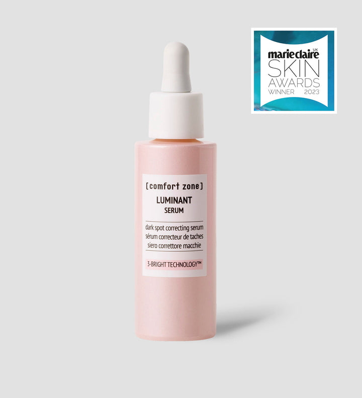 Flacon de Comfort Zone Luminant Serum, sérum correcteur de taches avec technologie 3-BRIGHT, sur fond gris clair. Flacon rose pâle avec un compte-gouttes blanc. Logo "marie claire SKIN AWARDS WINNER 2023" en haut à droite.