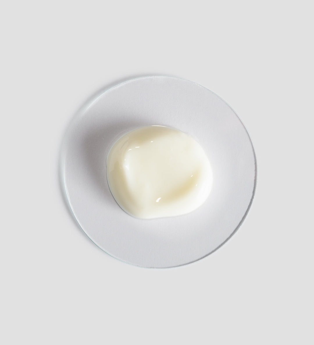 Texture du sérum fortifiant apaisant Remedy de Comfort Zone, montrant une petite quantité de produit blanc crémeux sur une plaque en verre transparente sur fond blanc clair.