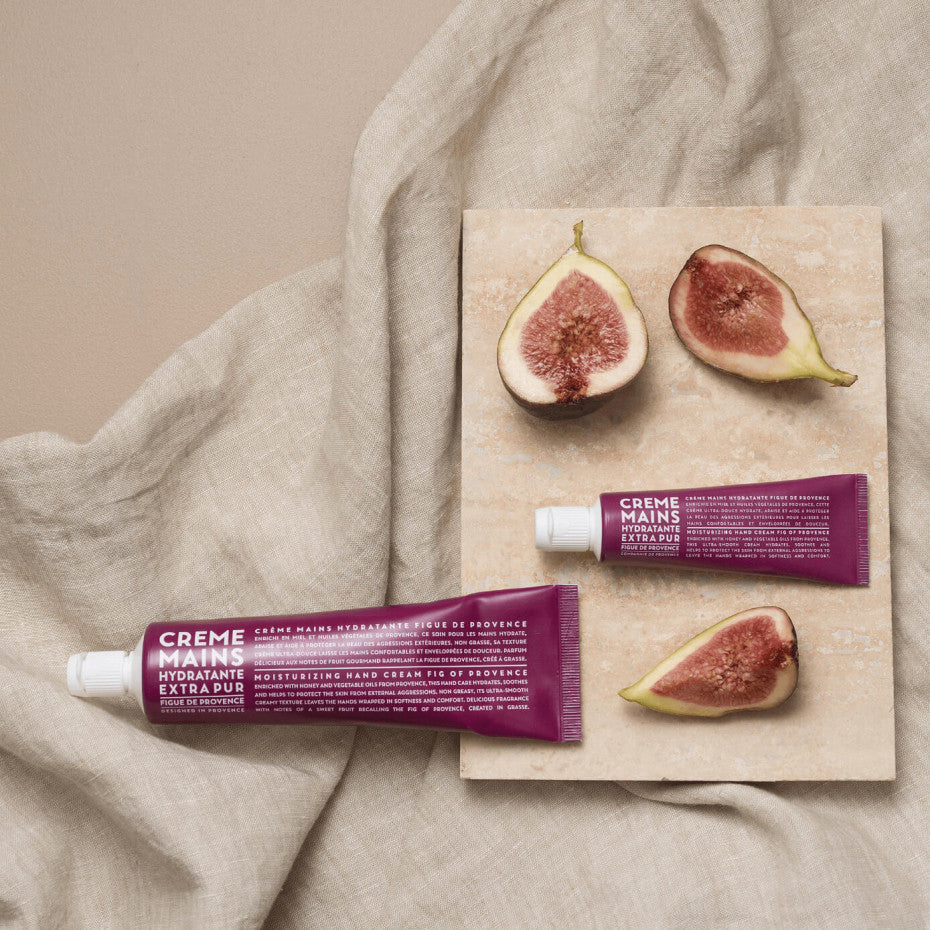 Crème mains hydratante Extra Pur à la figue de Provence de la marque Compagnie de Provence, présentée sur un tissu en lin avec des figues coupées et une plaque en pierre naturelle.