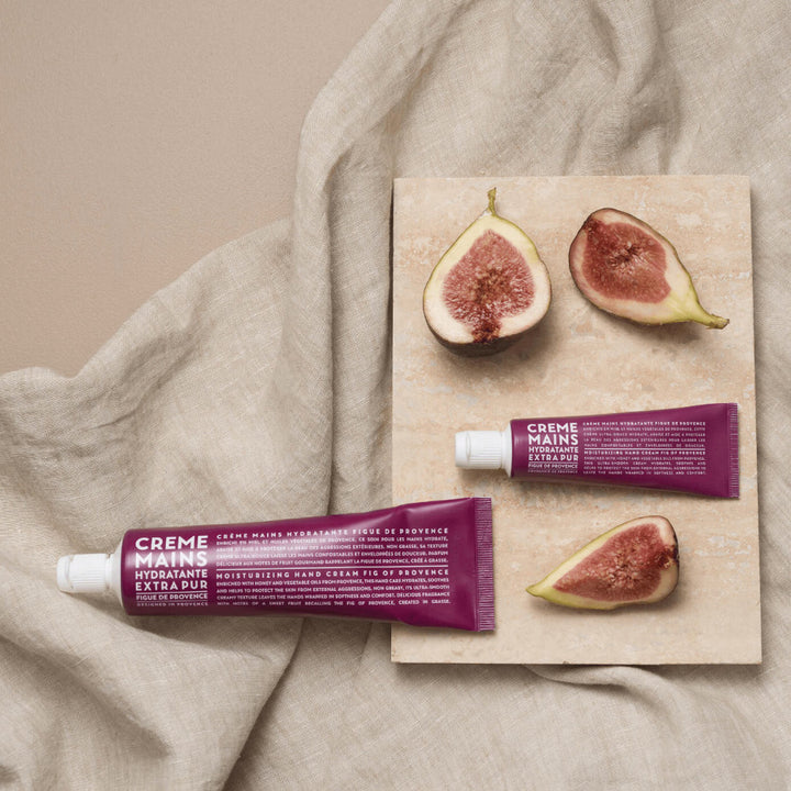 Crème mains hydratante Extra Pur à la figue de Provence de la marque Compagnie de Provence, présentée sur un tissu en lin avec des figues coupées et une plaque en pierre naturelle.