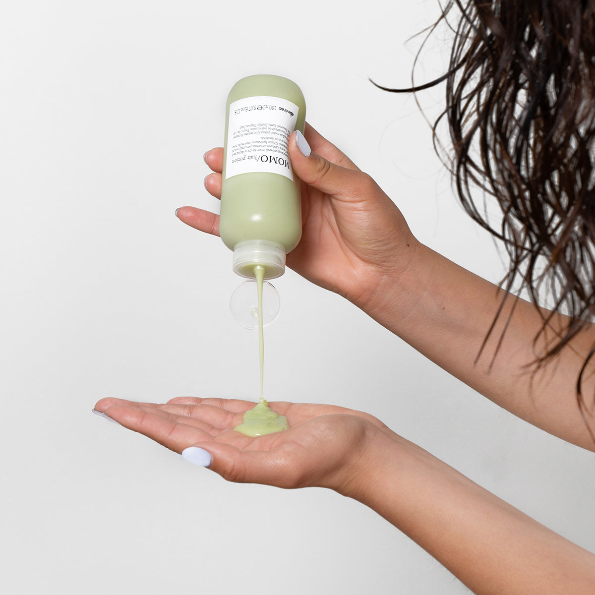 Application de la crème hydratante cheveux MOMO Hair Potion de Davines, versée depuis un flacon de 150 ml dans la paume d'une main, en arrière-plan des cheveux mouillés prêts à être coiffés