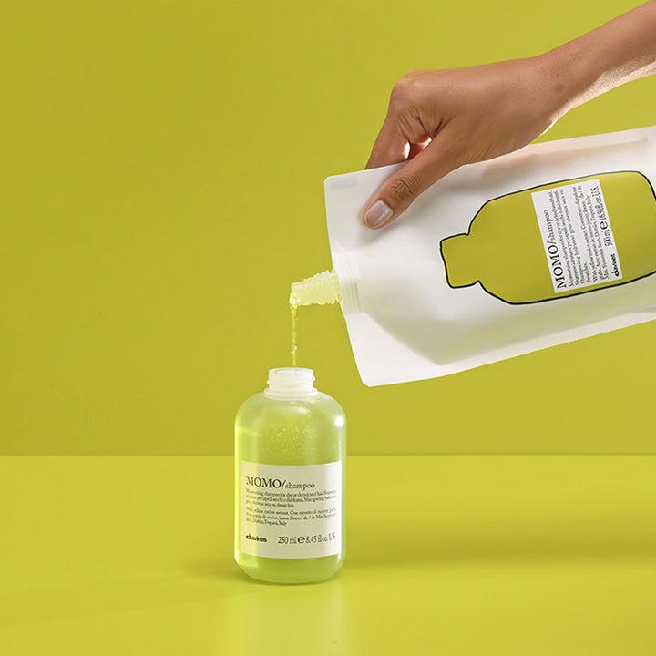 Remplissage du flacon 250 ml avec le shampoing hydratant Davines MOMO, versé depuis la recharge de 500 ml, texture fluide nourrissante enrichie en extrait de melon jaune, geste éco-responsable
