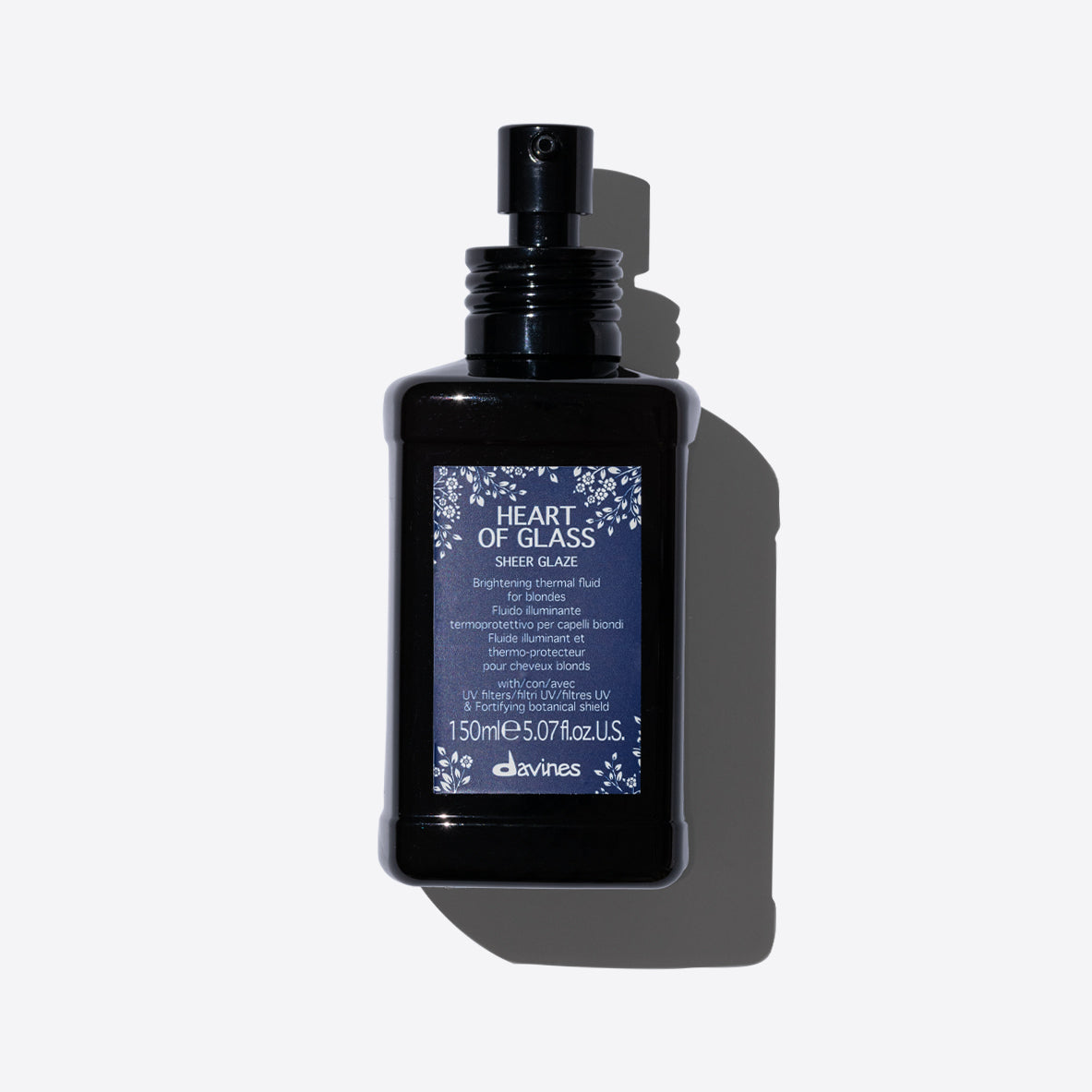 Flacon de fluide thermique illuminant pour cheveux blonds Davines Heart of Glass Sheer Glaze. Le flacon est noir avec une étiquette bleue, conçu pour protéger les cheveux blonds des dommages thermiques et des UV, tout en ajoutant de la brillance.