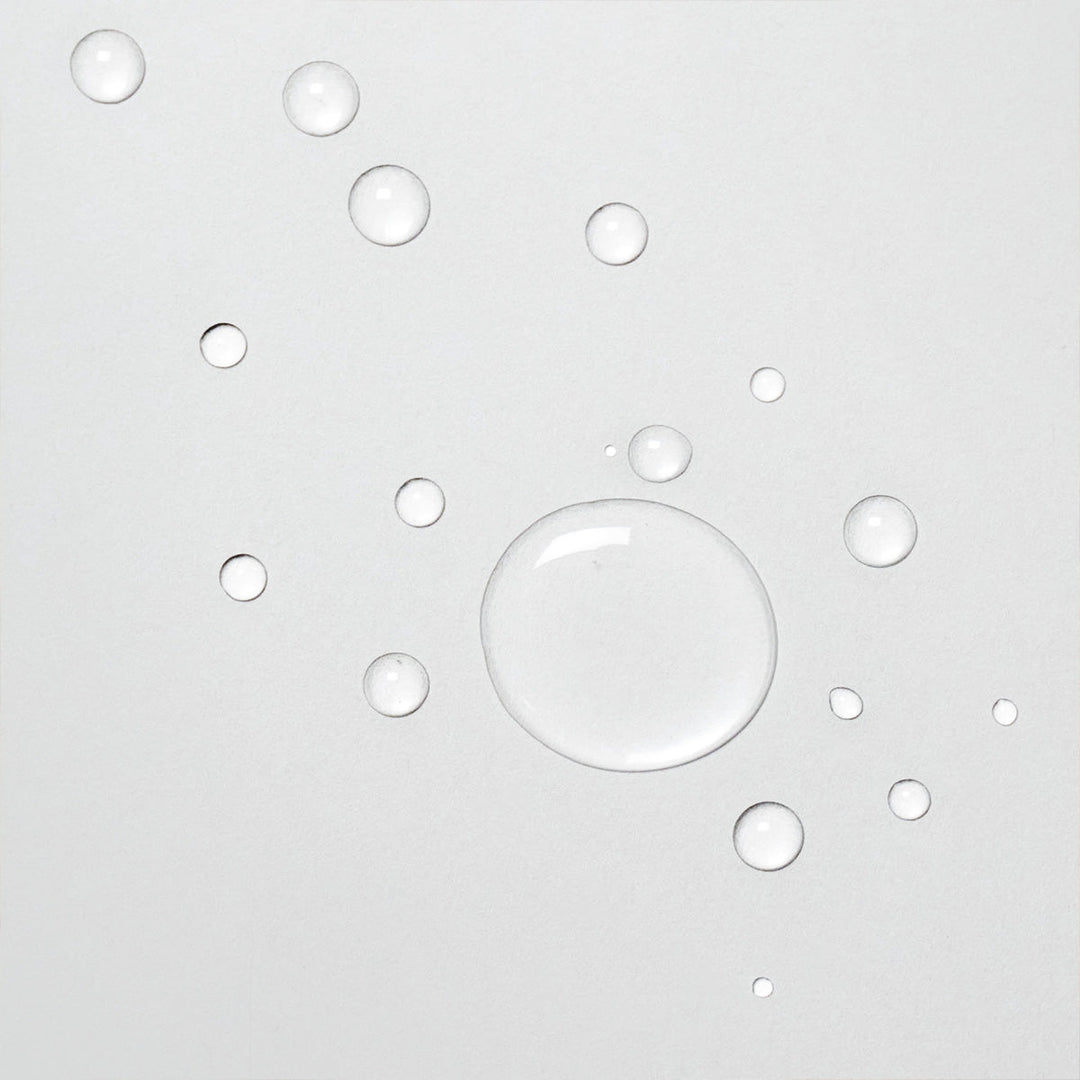 Gros plan sur des gouttes de Davines OI Liquid Luster sur une surface blanche. Les gouttes de liquide clair montrent la texture légère et fluide du produit, idéal pour une application douce et uniforme sur les cheveux.