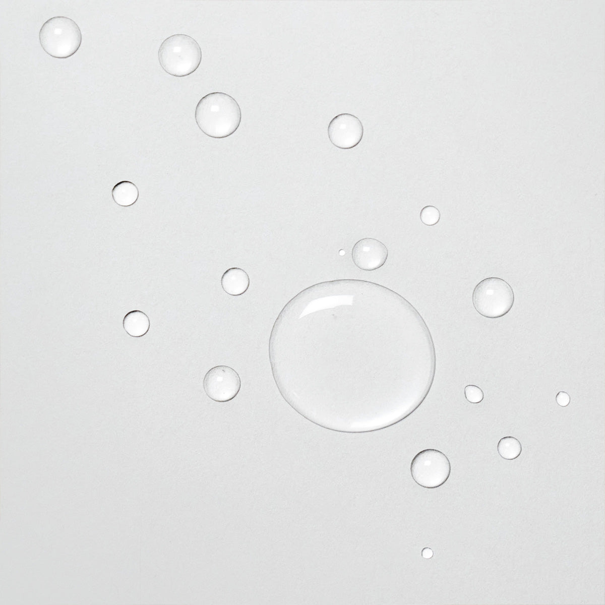 Gros plan sur des gouttes de Davines OI Liquid Luster sur une surface blanche. Les gouttes de liquide clair montrent la texture légère et fluide du produit, idéal pour une application douce et uniforme sur les cheveux.