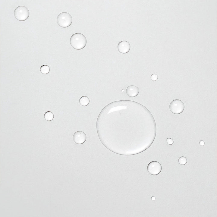 Gros plan sur des gouttes de Davines OI Liquid Luster sur une surface blanche. Les gouttes de liquide clair montrent la texture légère et fluide du produit, idéal pour une application douce et uniforme sur les cheveux.