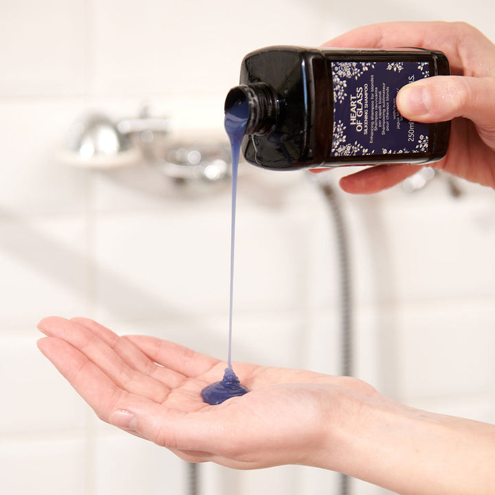 Application du shampooing sublimant Davines Heart of Glass. Le produit, de couleur bleue, est versé dans la paume de la main. Le flacon est noir avec une étiquette bleue, conçu pour revitaliser et protéger les cheveux blonds, tout en améliorant leur éclat et leur douceur.