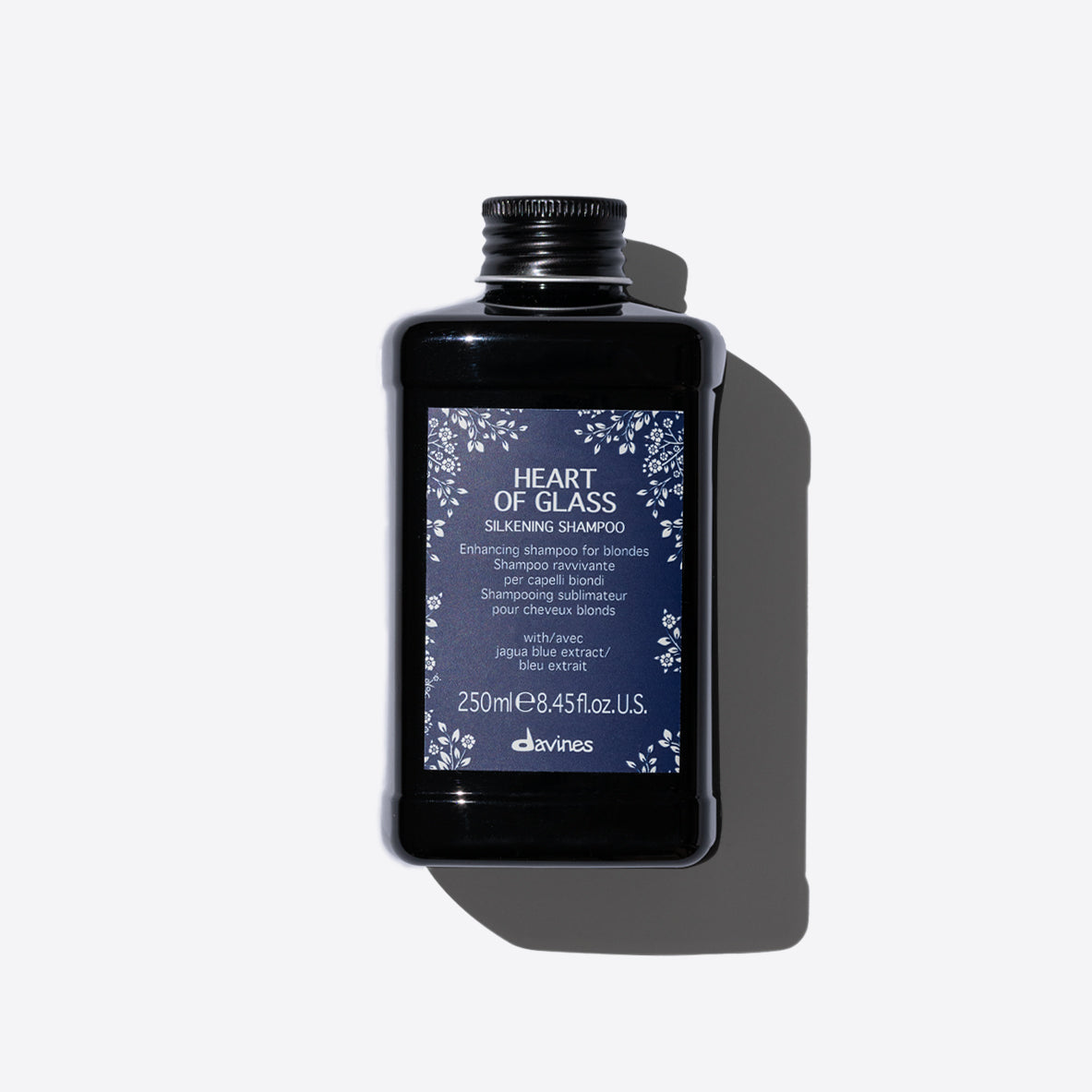 Flacon du shampooing sublimant Davines Heart of Glass. Le produit est contenu dans une bouteille noire avec une étiquette bleue. Conçu pour revitaliser et protéger les cheveux blonds, ce shampooing sublime leur éclat et leur douceur grâce à l'extrait de jagua bleu. Contenance de 250 ml.