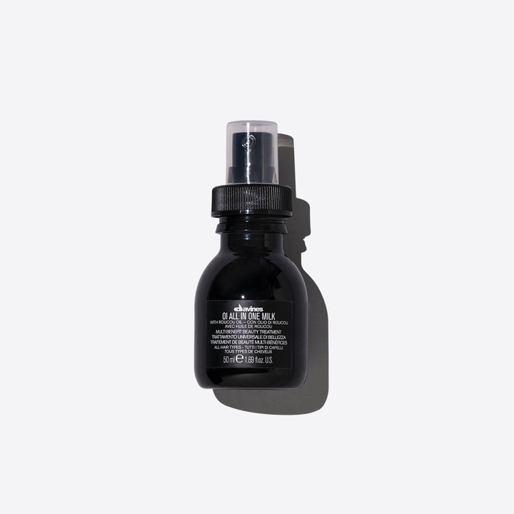 Une bouteille noire élégante de 50 ml du lait multifonction "OI All In One Milk" de Davines. Le produit, présenté en format spray, est formulé avec de l'huile de Roucou, connue pour ses propriétés nourrissantes et protectrices. Ce traitement beauté multifonctionnel est conçu pour hydrater, démêler, contrôler les frisottis et ajouter de la brillance aux cheveux. Parfait pour un usage quotidien, il convient à tous les types de cheveux et offre un soin complet en un seul geste.