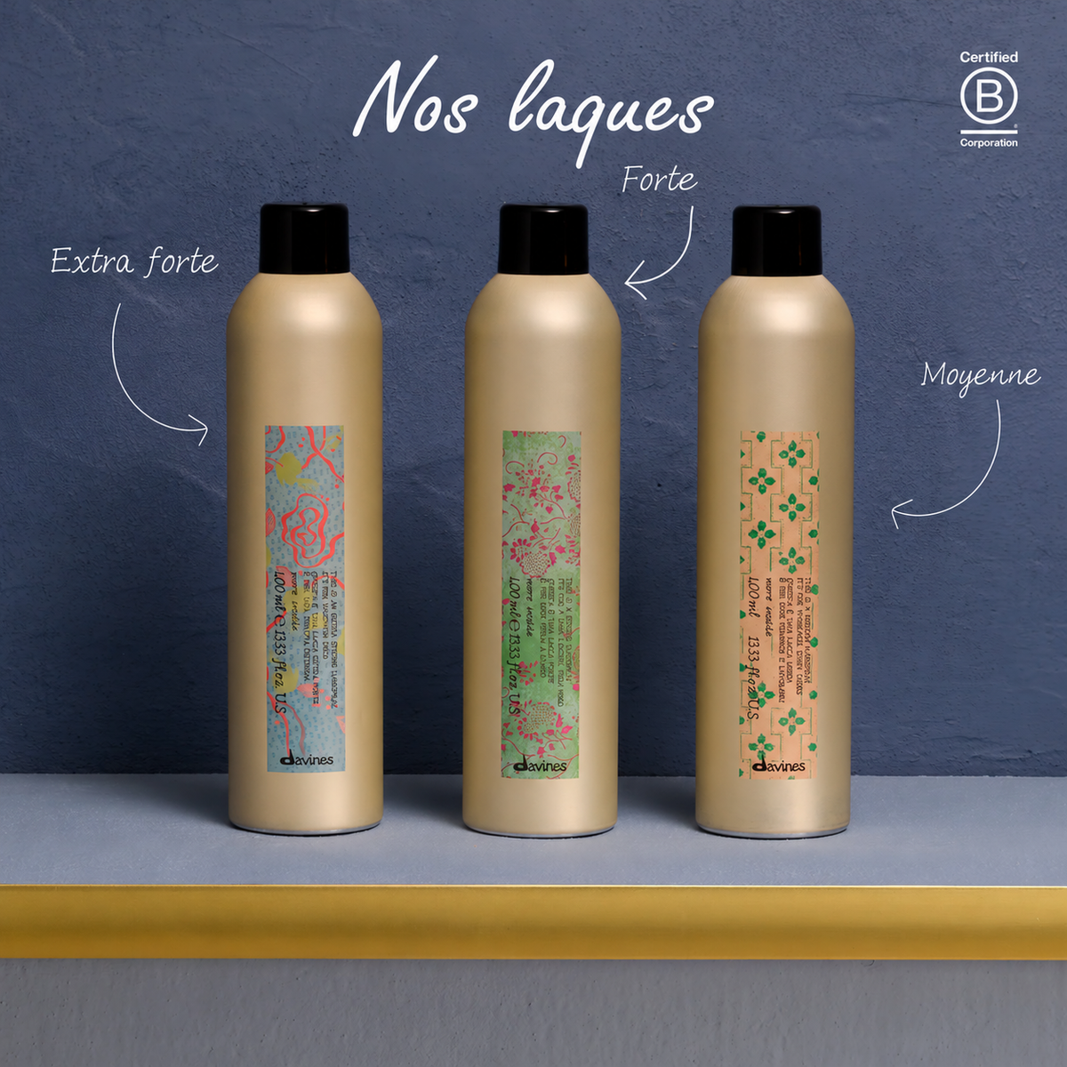 Trois laques Davines More Inside sur une étagère devant un mur bleu ; les flèches en français indiquent les fixations extra forte, forte et moyenne.