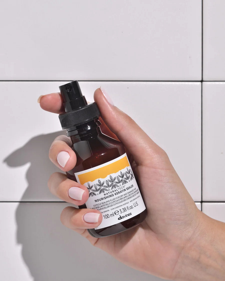 Davines Nourishing Keratin Sealer 100 ml – flacon tenu en main devant un carrelage blanc