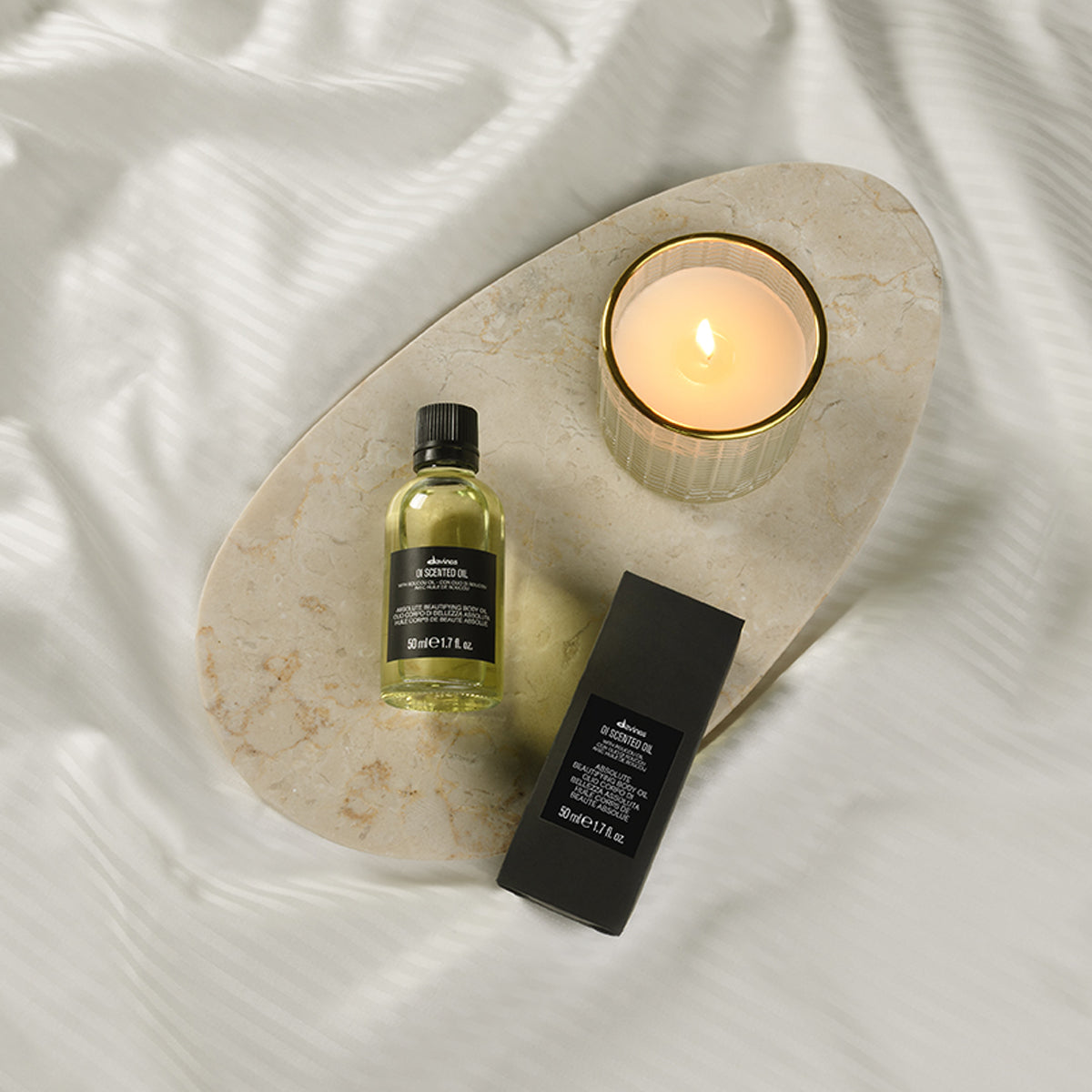 Flacon et étui OI Scented Oil 50 ml sur un plateau en pierre avec une bougie, photo officielle Davines.