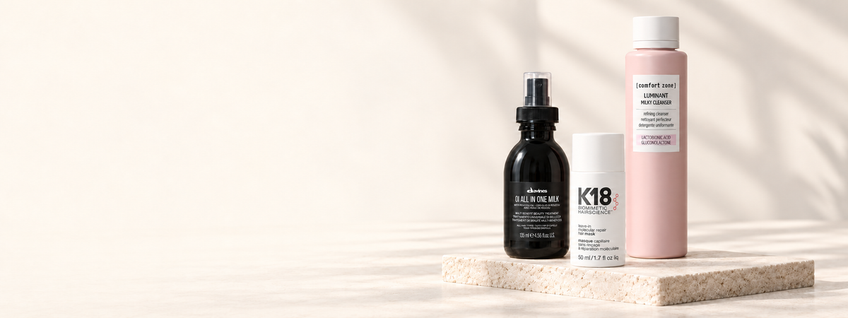 Soins Davines OI All In One Milk, masque K18 Molecular Repair et nettoyant Comfort Zone Luminant, présentés sur un socle en pierre claire.
