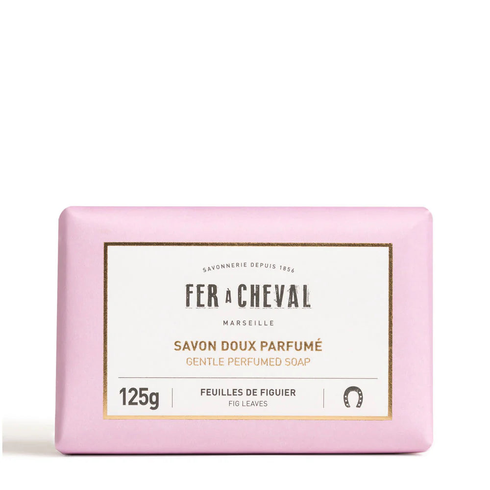 Image d'un savon doux parfumé de la marque Fer à Cheval, parfum feuilles de figuier, de 125g. Le savon est emballé dans un papier de couleur rose pastel avec une étiquette blanche au centre portant le nom de la marque, le type de produit et son parfum. Le design simple et élégant reflète la qualité artisanale et naturelle du produit.