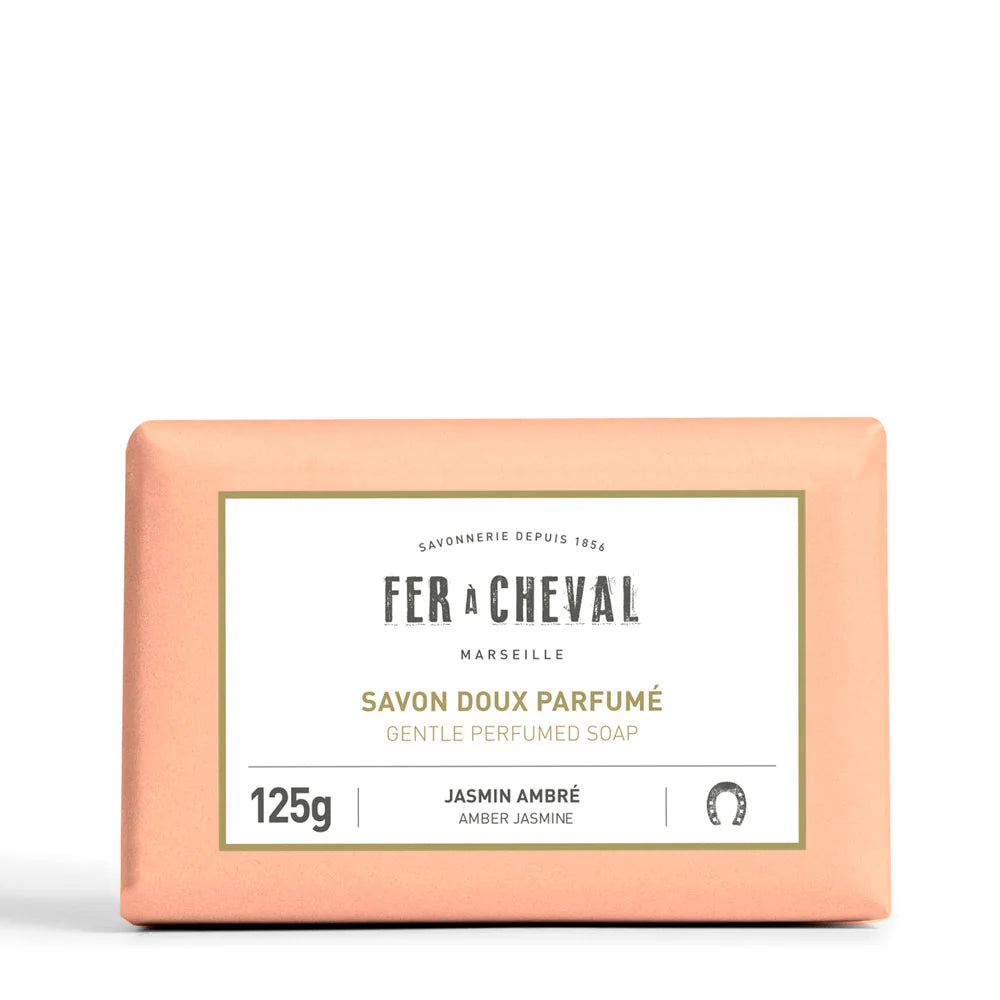 Image d'un savon doux parfumé de la marque Fer à Cheval, parfum jasmin ambré, de 125g. Le savon est emballé dans un papier de couleur pêche avec une étiquette blanche au centre portant le nom de la marque, le type de produit et son parfum. Le design simple et élégant reflète la qualité artisanale et naturelle du produit.