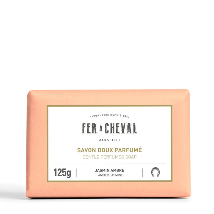 Image d'un savon doux parfumé de la marque Fer à Cheval, parfum jasmin ambré, de 125g. Le savon est emballé dans un papier de couleur pêche avec une étiquette blanche au centre portant le nom de la marque, le type de produit et son parfum. Le design simple et élégant reflète la qualité artisanale et naturelle du produit.