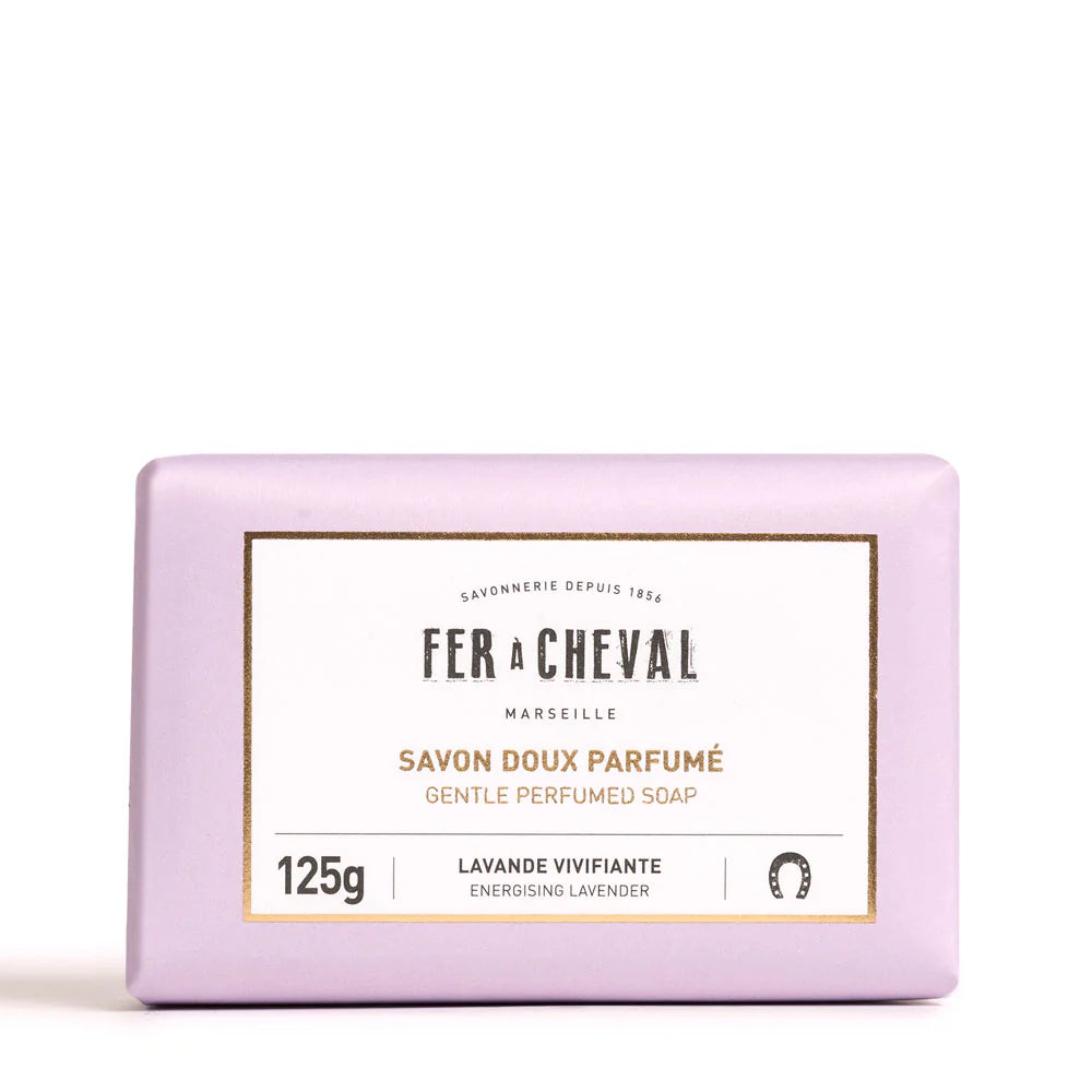 Image d'un savon doux parfumé de la marque Fer à Cheval, parfum lavande vivifiante, de 125g. Le savon est emballé dans un papier de couleur lavande avec une étiquette blanche au centre portant le nom de la marque, le type de produit et son parfum. Le design simple et élégant reflète la qualité artisanale et naturelle du produit, avec des mentions en français et en anglais.