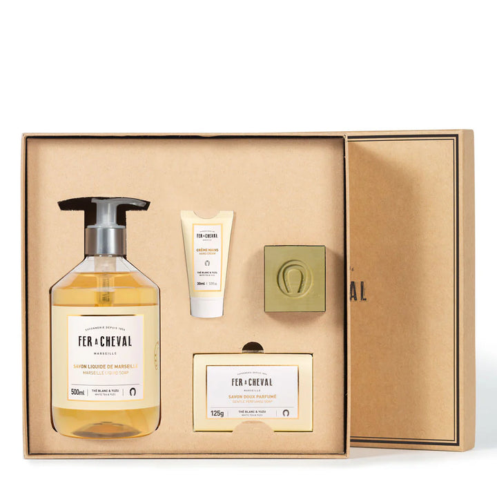 Image montrant le contenu du coffret élégant Thé Blanc Yuzu de la marque Fer à Cheval. Le coffret contient un flacon de savon liquide de Marseille (500ml), un tube de crème pour les mains (30ml), un savon doux parfumé (125g) et un savon de Marseille classique. Tous les produits sont parfumés au thé blanc et yuzu.