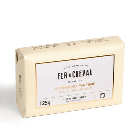 Image d'un savon doux parfumé de la marque Fer à Cheval. L'emballage est de couleur beige avec l'inscription "Savon Doux Parfumé" en lettres dorées. Le savon, parfumé au thé blanc et yuzu, pèse 125g et est marqué du logo Fer à Cheval.