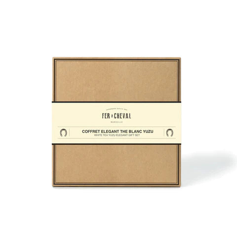 Image d'un coffret cadeau élégant de la marque Fer à Cheval. Le coffret en carton brun est entouré d'une bandelette beige indiquant "Coffret Elegant Thé Blanc Yuzu". Ce coffret contient des produits parfumés au thé blanc et yuzu.