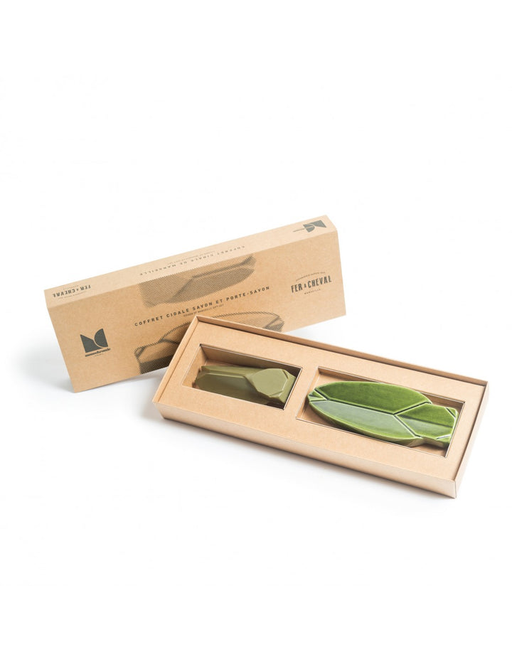 Image du coffret de savon cigale et porte-savon issu de l'association entre Fer à Cheval et Monochromic. Le coffret en carton contient un savon en forme de cigale et un porte-savon assorti, tous deux de couleur verte. Le savon et le porte-savon sont présentés dans un emballage élégant et minimaliste.